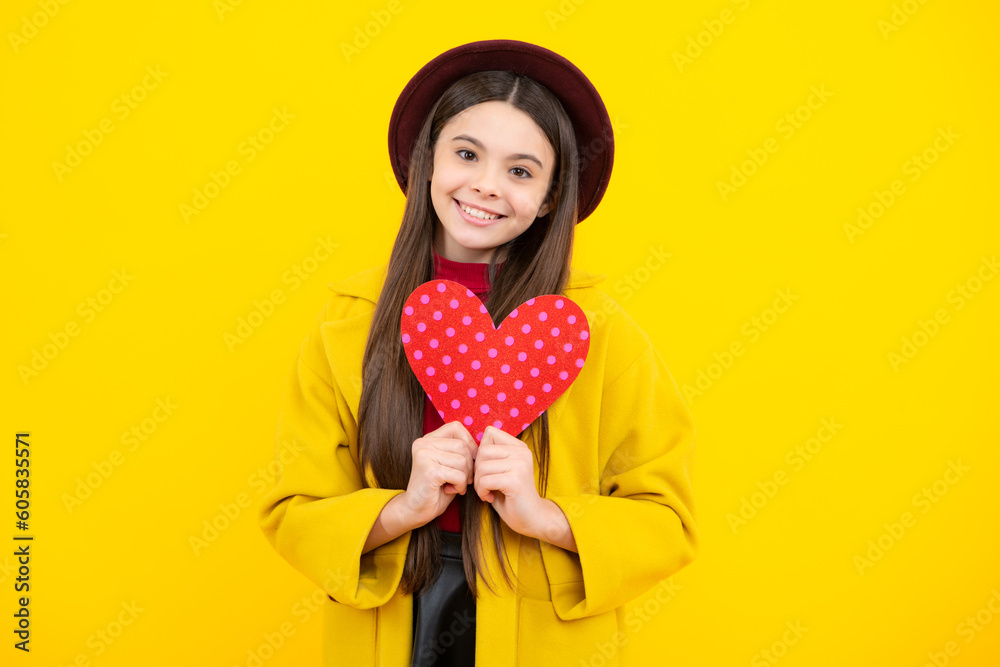 Happy teenager portrait. Cheerful lovely romantic teen girl hold red heart symbol of love for valentines day isolated on yellow background. Smiling girl. Happy teenager portrait. Cheerful lovely romantic teen girl hold red heart symbol of love for valentines day isolated on yellow background. Smiling girl.