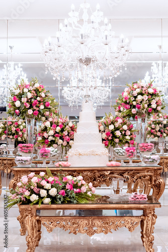 a golden wooden table, with a wedding cake in the center, decorated with vases of rose flowers and sweets