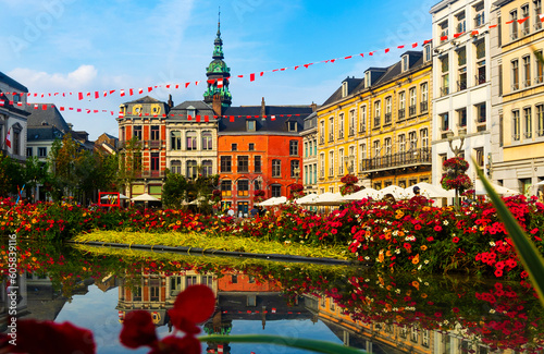 Picturesque summer view of flowering central Grand Place square in Mons overlooking baroque belfry of Roman Catholic Church of St. Elizabeth towering over colorful residential townhouses, Belgium