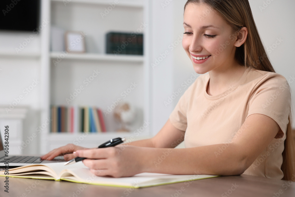 Online learning. Teenage girl writing in notebook near laptop at home Online learning. Teenage girl writing in notebook near laptop at home