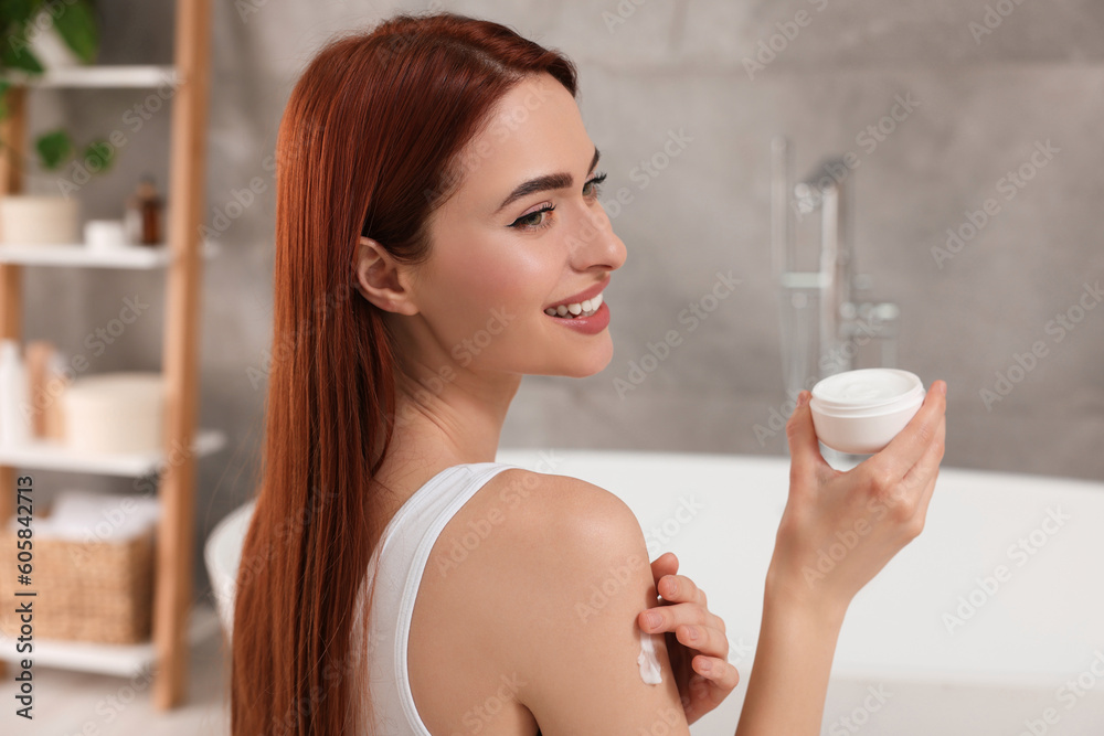 Beautiful young woman applying body cream onto shoulder in bathroom Beautiful young woman applying body cream onto shoulder in bathroom