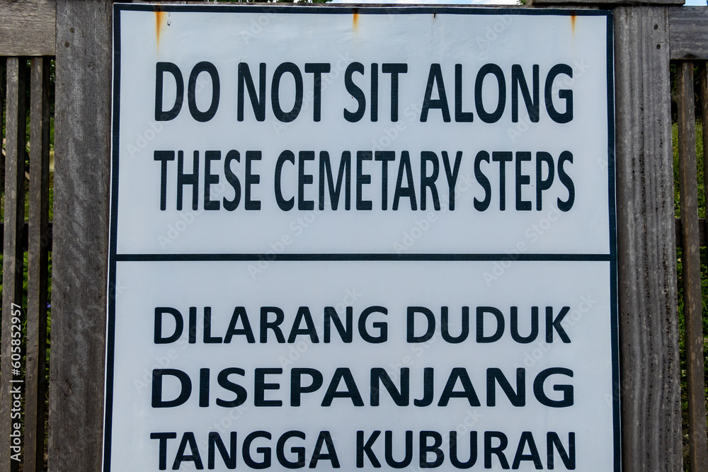 Canggu, Bali, Indonesia, A sign on the beach in English and Indonesian says not to sit on cemetery steps. Canggu, Bali, Indonesia, A sign on the beach in English and Indonesian says not to sit on cemetery steps.