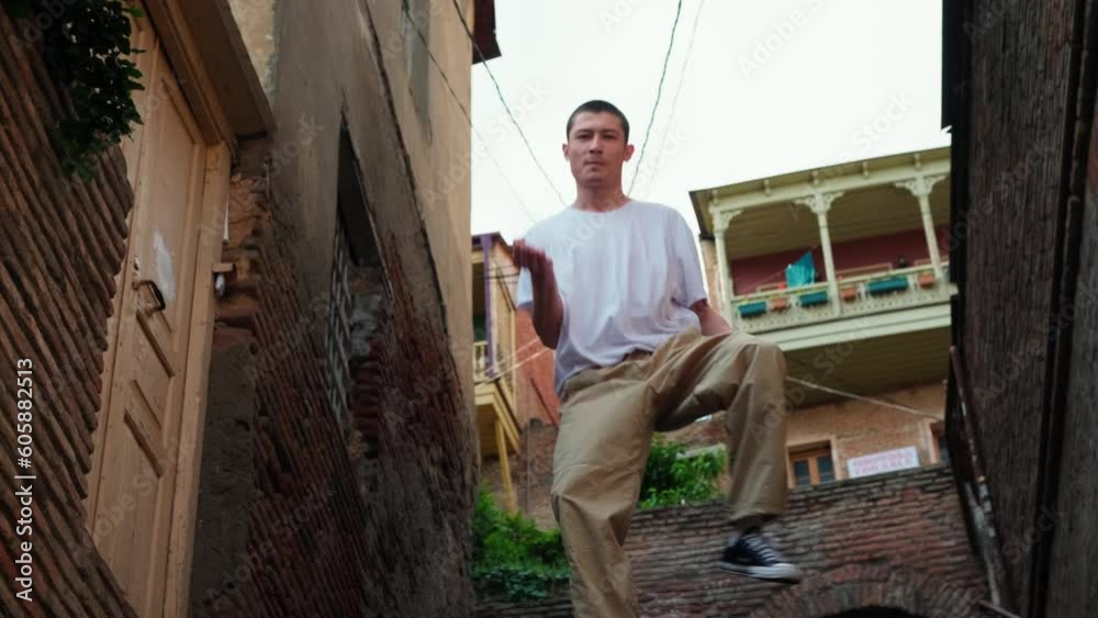 A guy in a white T-shirt defiantly dances a modern dance on the streets of the old city. Historical streets of Tbilisi. A young dancer improvises in a dance and steps up the steps. Freestyle, hip hop. A guy in a white T-shirt defiantly dances a modern dance on the streets of the old city. Historical streets of Tbilisi. A young dancer improvises in a dance and steps up the steps. Freestyle, hip hop.