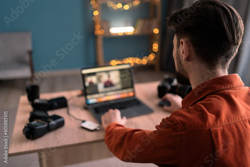 Young creative man work on laptop computer editing photos at home office. Male photographer at home workplace.