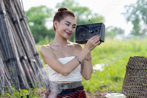 Thai lady beautiful dressing traditional northern style listening radio music from transistor a have happy joyful smiling in rice field and cooking for dinner.Retro radio and young women outdoors