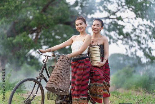 Beautiful girls wearing Thai traditional dress in the countryside takes her bicycle back from the rice fields and random catch fish on bike. One holding a vintage tiffin container.Portrait smile