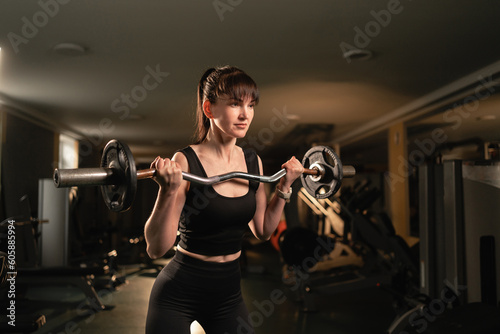 Sportswoman exercise with light barbell in the gym. Determined fitness woman training with heavy weights in a fitness club.
