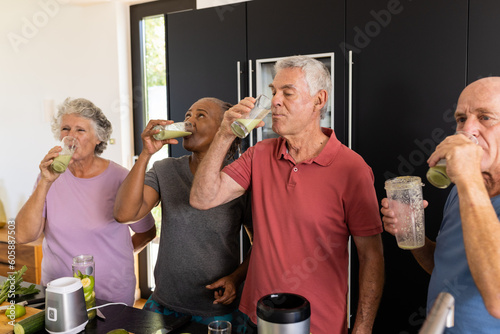 Happy diverse senior friends drinking healthy smoothies together in kitchen