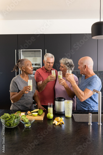 Happy diverse senior friends talking and preparing healthy smoothies together in kitchen