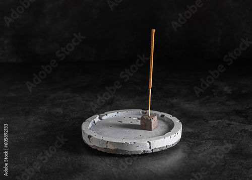 Incense round stand with incense stick on a dark background, selective focus, copy space, low key. Meditating, relaxation, aromatherapy. 
