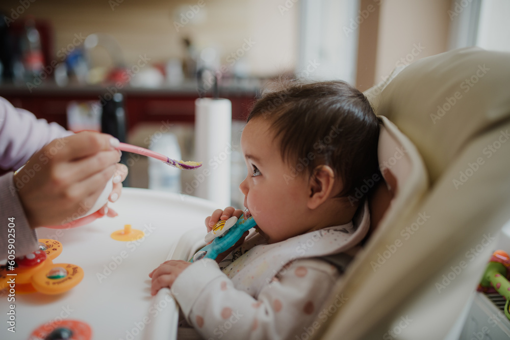 Profile portrait of baby sitting at highchair and eating from spoon Profile portrait of baby sitting at highchair and eating from spoon