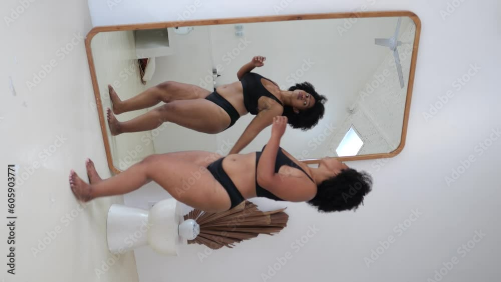 Plus-size black multiethnic body-positive woman dances in front of mirror. Happiness life enjoyment of your body, pleasure of being yourself. Normalization of diverse body shapes, genders. vertical
