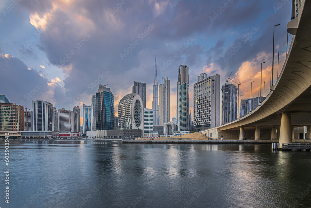 Sunset with a cloudy sky over the financial district of Dubai. City skyline in business center with office buildings and skyscrapers around Burj Khalifa. Street with a bridge over the harbor