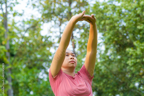 Young Asian woman in sportswear stretches before exercising in the park for a healthy lifestyle. Young healthy woman warming up outdoors. Healthy lifestyle concept. © scentrio