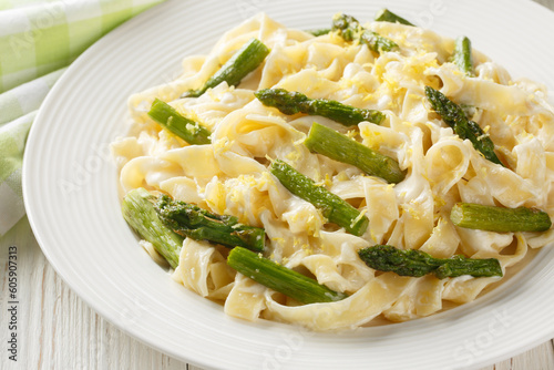 Delicious fettuccine pasta with asparagus, lemon in creamy parmesan sauce close-up in a plate on the table. Horizontal