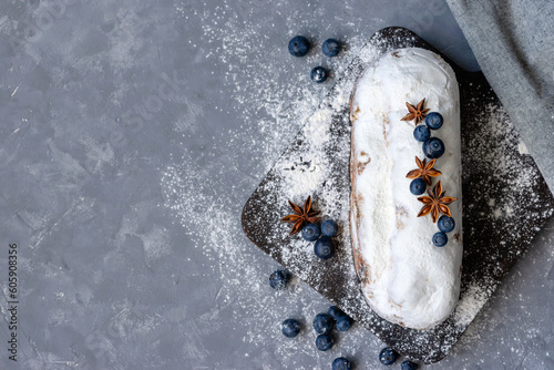 Aesthetic holiday Christmas dessert, stollen decorated with blueberry, raisins, sugar powder on wooden board on gray background, authentic homemade German bakery, copy space