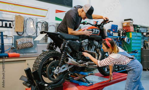 Mechanic couple team reviewing engine of custom motorbike over platform on factory
