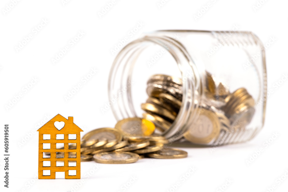 Simaolic wooden house and gold coins pouring out of a glass jar on a white background Simaolic wooden house and gold coins pouring out of a glass jar on a white background