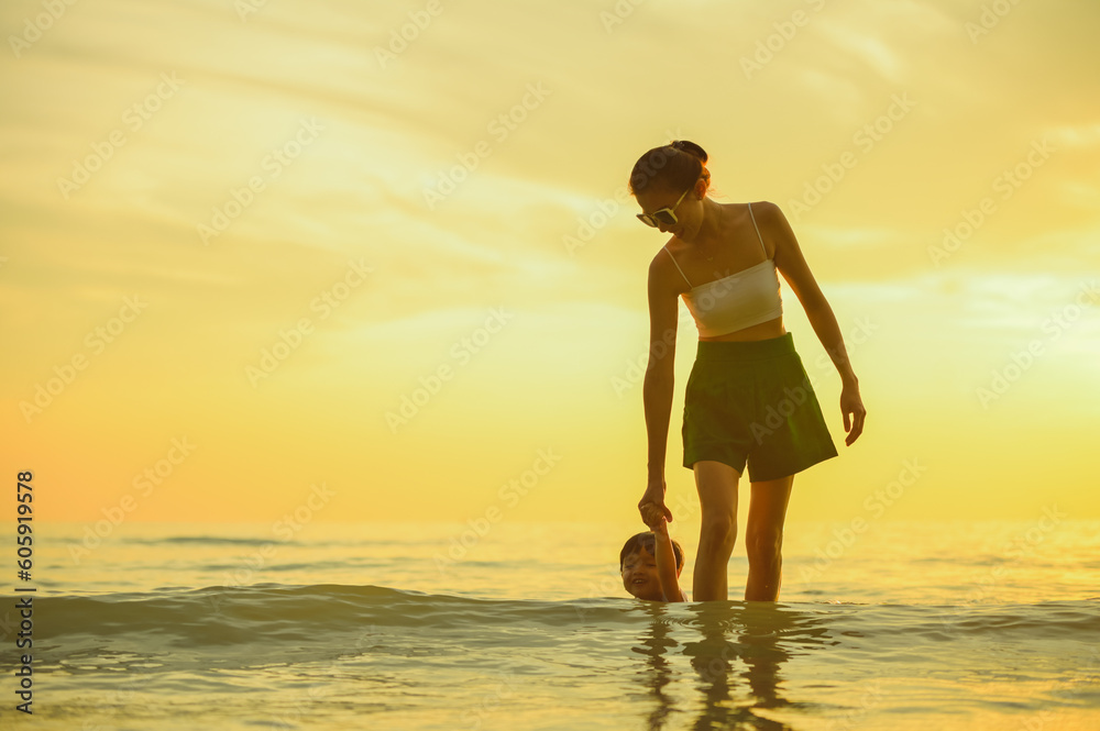 Happy family resting at beach in summer, Mother and baby boy feet at the sea foam at the sunlight water is moving