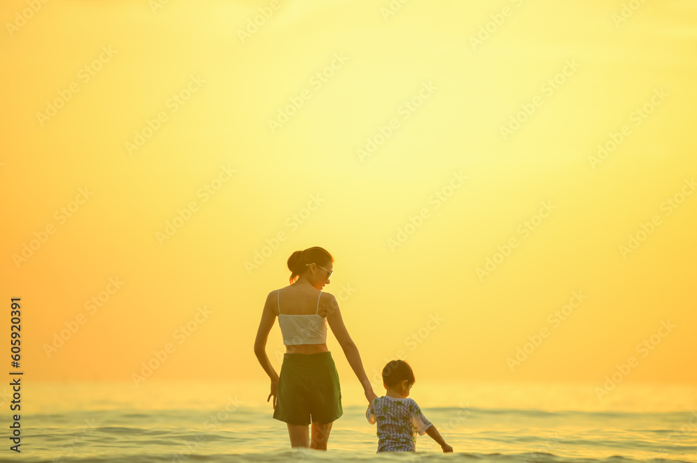 Happy family resting at beach in summer, Mother and baby boy feet at the sea foam at the sunlight water is moving