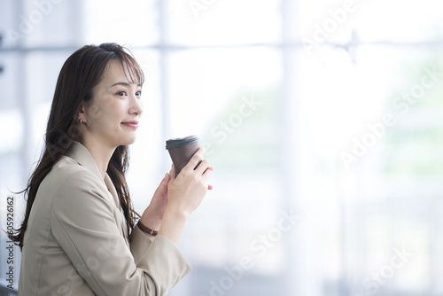 Beautiful Asian woman in a suit in an office building, taking a break for a cup of coffee. © kapinon