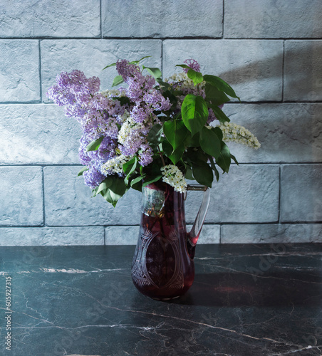 Still life with lilacs in a glass vase on a dark marble table. Concept freshness of fragrance.