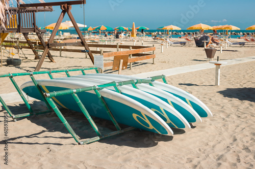 Surfboard storage on sandy beachon for hire rent at beach Viserbella Italy on background of beach umbrellas and sunbeds. International Surfing Day