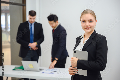 Young happy businesswoman looking into camera holding tablet Confident smiling business boss standing in office at team meeting Portrait of confident business woman with colleague in conference room