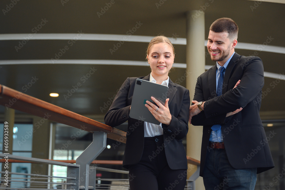 Attractive business man and business woman happy smile Use digital tablets to look at market data and talk while walking in the office. business conversation Attractive business man and business woman happy smile Use digital tablets to look at market data and talk while walking in the office. business conversation
