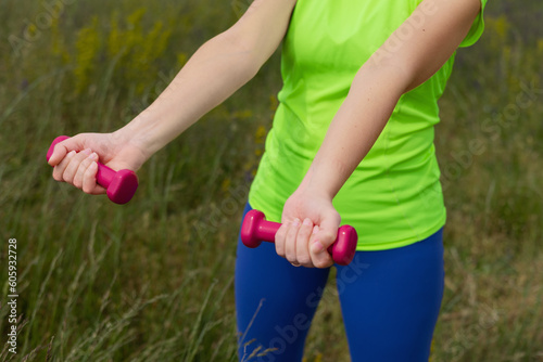 Closeup of hands woman with pink dumbbells in bright colored sportswear doing exercise.