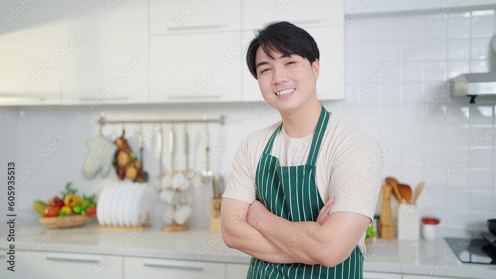 Young asian men wearing apron smiling to camera whlie standing with arms crossed and confident in kitchen room at home Young asian men wearing apron smiling to camera whlie standing with arms crossed and confident in kitchen room at home
