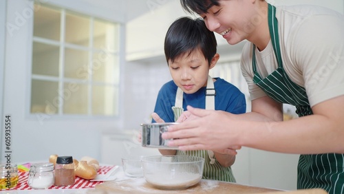 Фотография Asian single father teaching son to sift flour for cooking or baking spending time on holidays together in kitchen room at home