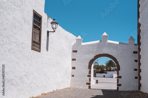 Typical Canary Islands street with white houses, green wooden doors and windows and colorful flowers in Teguise village, Canary Islands, Spain.