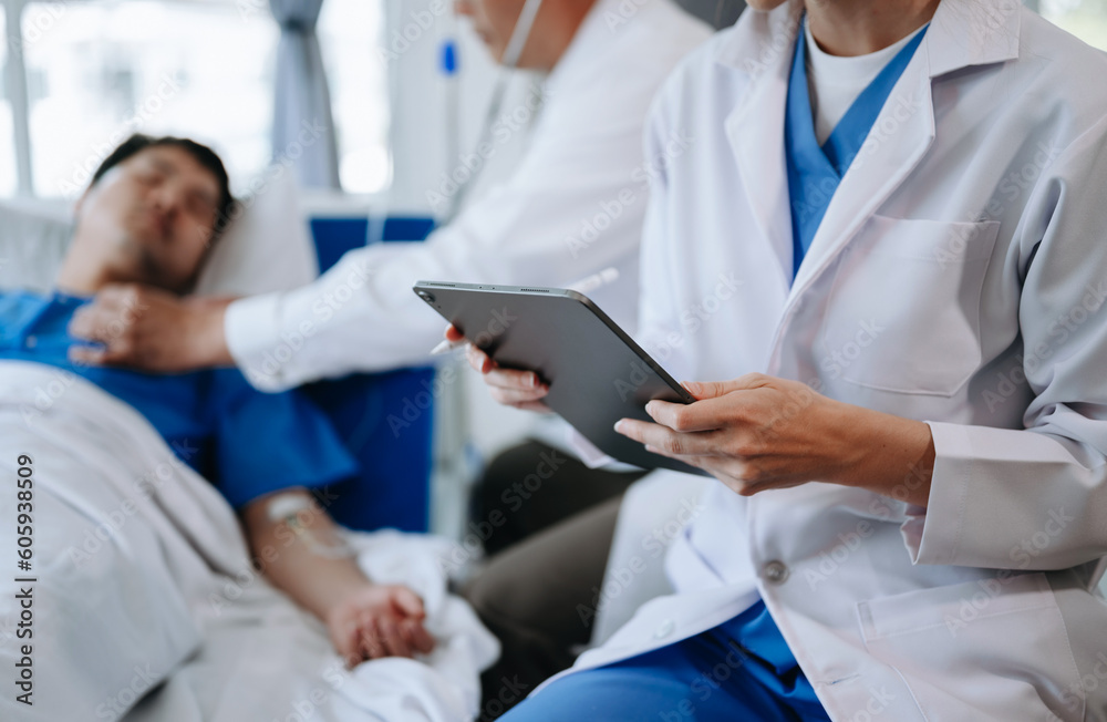 Two doctors talking to a patient lying in his bed with receiving saline solution in a hospital Two doctors talking to a patient lying in his bed with receiving saline solution in a hospital