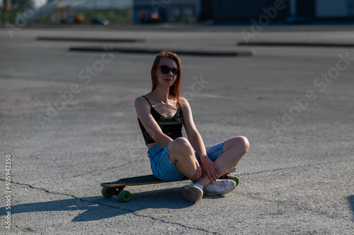 Young caucasian woman sitting on a longboard and relaxing outdoors. 