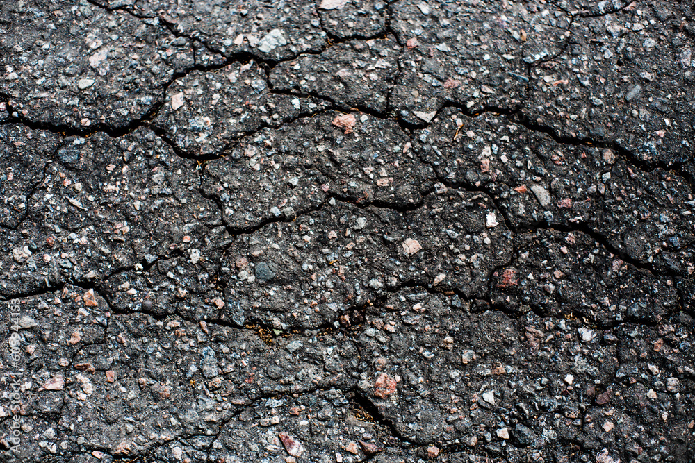 A network of black cracks on the asphalt surface. Road texture with weathered surface, showcasing the effects of time and wear A network of black cracks on the asphalt surface. Road texture with weathered surface, showcasing the effects of time and wear