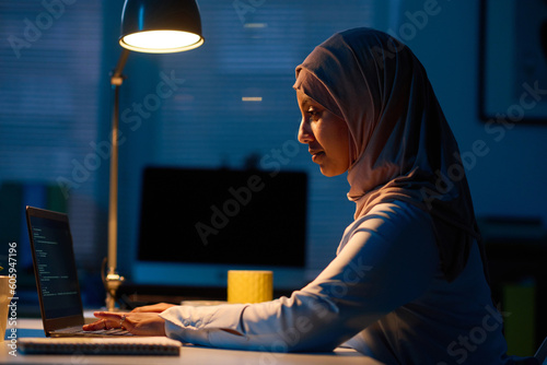 Side view of muslim woman working online on laptop in office during deadline