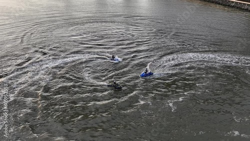 An aerial view over the Spuyten Duyvil Creek on a cloudy day. There are three people on jet skis floating in the creek. The camera is tilt down over the trio and is stationary, filming in slow motion. photo