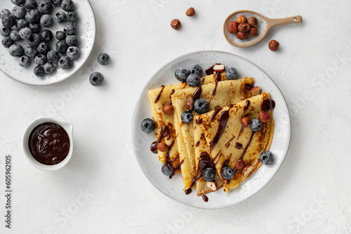 Crepes, blinis or thin pancakes with blueberries, hazelnuts and chocolate sauce on a white plate at white stone table. Maslenitsa traditional festival meal. Delicious breakfast.