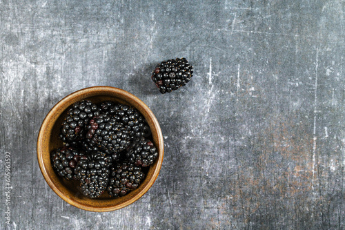 Ceramic bowl with fresh blackberries on a grey background. Concept of healthy food and lifestyle. Macro photography of blackberries. Closeup view. Dark food photography