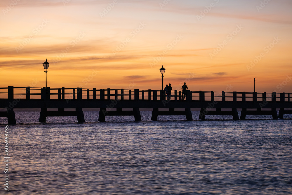 Pedestrians on footbridge at sunset above calm water