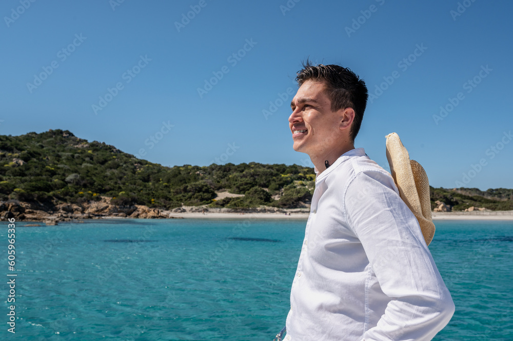 Side view of cheerful male with straw hat in summer outfit standing on deck of modern catamaran sailing in sea during summer vacation