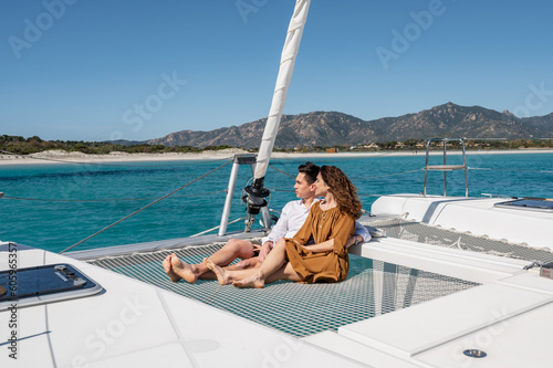 Side view of couple in love sitting on net while sailing on yacht and enjoying summer vacation in sea