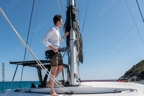 Side view of male standing with rope near mast on sailing catamaran in sea