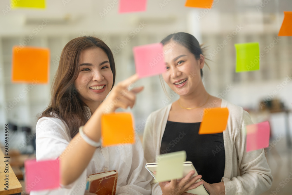 Asian businesswoman sharing opinions and analyzing notes on glass with colleagues in office. Asian businesswoman sharing opinions and analyzing notes on glass with colleagues in office.