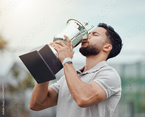 Man, tennis and kissing trophy in celebration for winning, success or achievement on the court. Male person, athlete or winner in love or kiss on champion award, prize or reward for sport competition photo