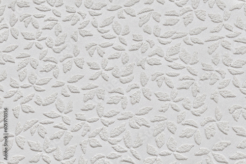 White paper wallpaper texture with abstract floral repeating pattern close up. Plastered embossed wall.