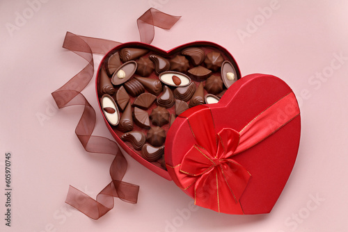 Heart shaped box with delicious chocolate candies and ribbon on pale pink background, flat lay © New Africa