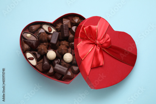 Heart shaped box with delicious chocolate candies on light blue background, top view