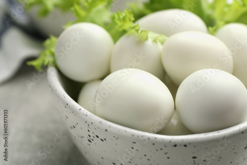Peeled boiled quail eggs in bowl on grey table, closeup